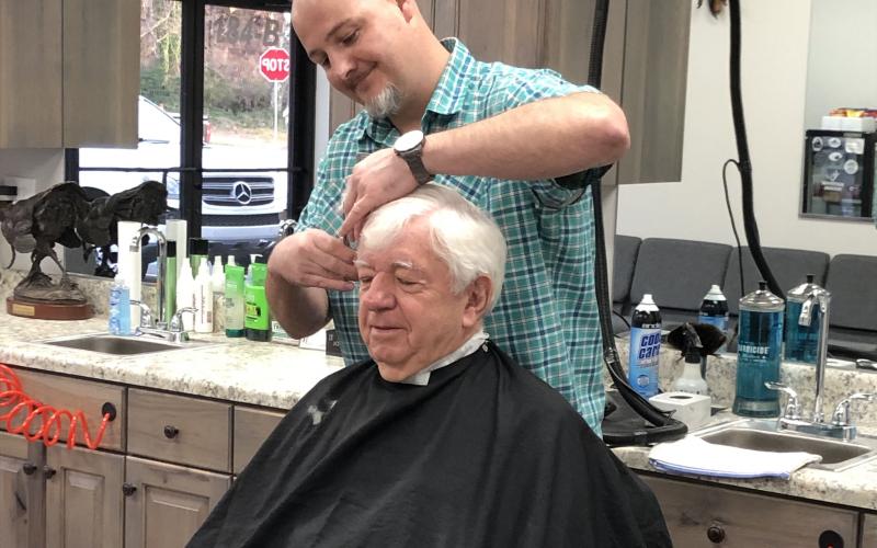 Pharmacist Ray Black sits for the first-ever haircut from Nathan McIntyre at Nate’s Barbershop, which opened Monday in Black’s new development, Cleveland Drug Plaza on West Kytle Street. Read more about the changes on 7A. (Photo submitted)