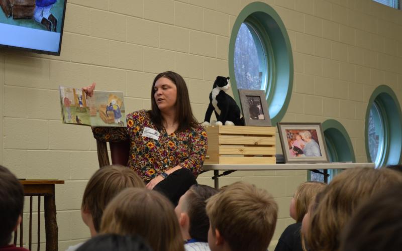 Author Laurel Hamby reads her book, Kiki Comes Home, to fourth and fifth grade students at Mt. Yonah Elementary School. Beside her is a stuffed cat that looks like Kiki, and photos of the real Kiki. (Photo/Samantha Sinclair)