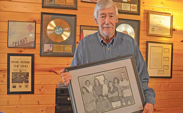 Gary Donehoo holds a photo of him, Alan Walden and Eddie Floyd with Lynyrd Skynyrd in front of his wall of memorabilia of the band. “They were all good guys,” Donehoo said. “The original band, they were hungry, they all came from west Jacksonville… they knew the only way out was education, music or sports.” (Photo/Samantha Sinclair)
