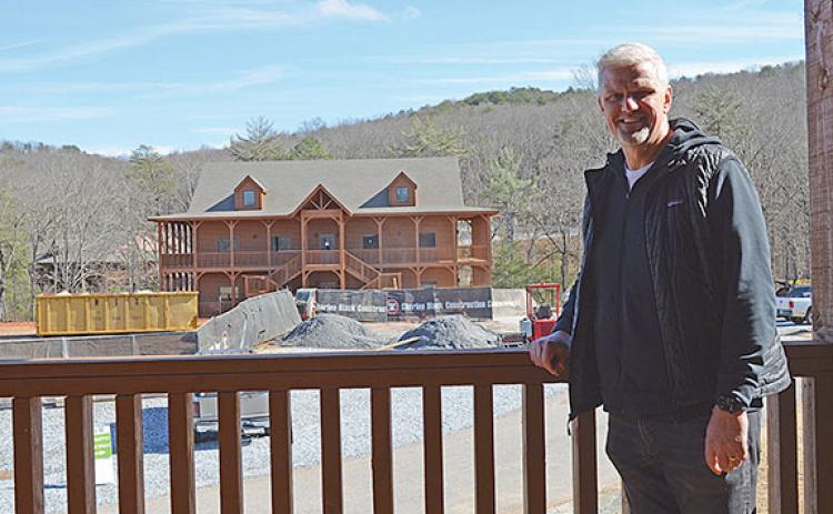 Jon Estes stands on the balcony of the Green Wood cabin as construction concludes on the Blue Creek cabin across the road. (Photo/Samantha Sinclair)