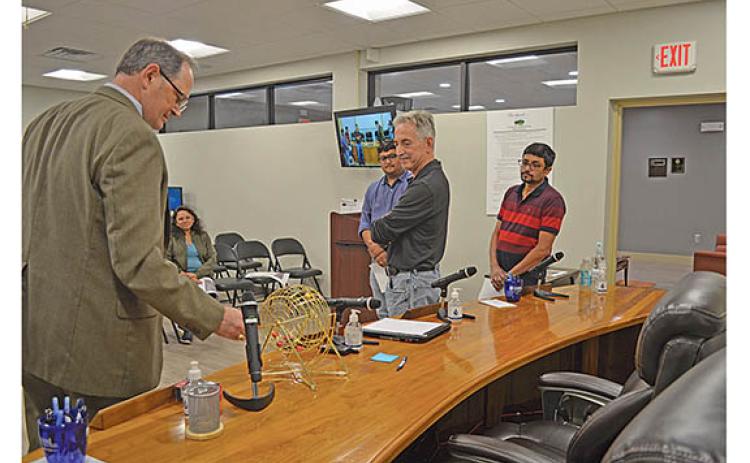 As City Auditor Wayne Tuck spins the bingo cage, package store applicants Sarthi Gandhi, Gerald Singer and Garth Gandhi watch to see which ball is selected in the package store lottery. (Photo/Samantha Sinclair)