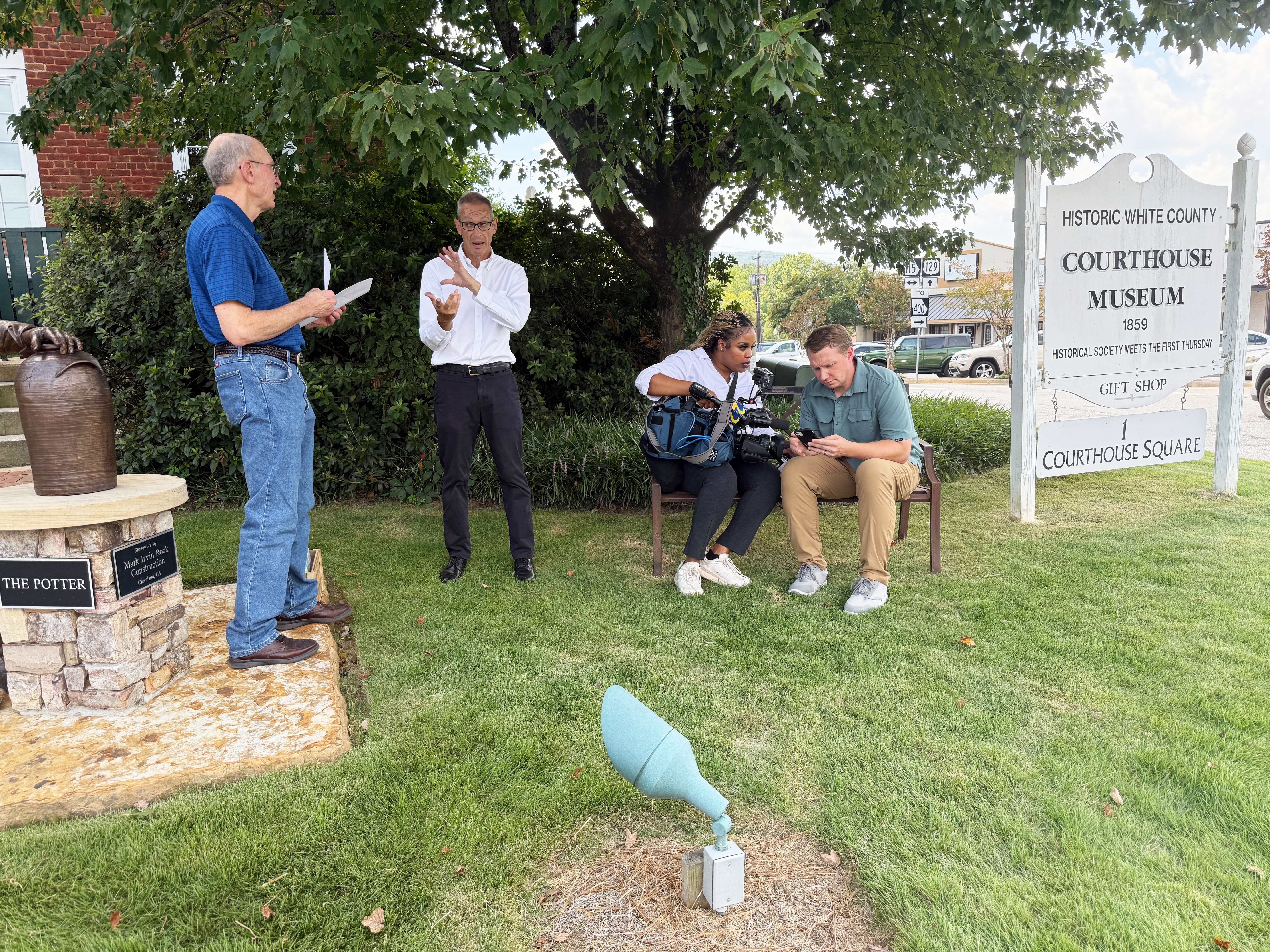 Foundational Literacy co-founder John Aiken, left, speaks with WSB TV reporter Berndt Peterson, while videographer Deja Pino, seated, left, records Joe Edlhuber on the grounds of the White County Historic Museum Aug. 26. LINDA ERBELE/WCN