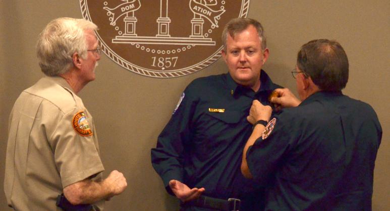 New county Fire Chief Seth Weaver (center) stands as his predecessor, Norman Alexander (right), carries out a ceremonial pinning with Sheriff Neal Walden.