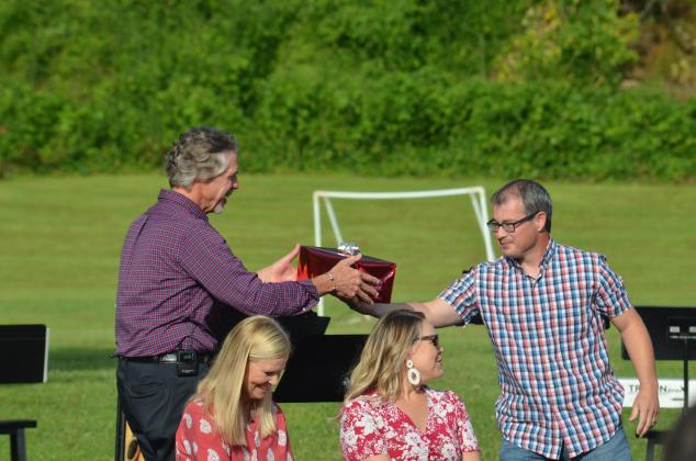 Nathan Adams (right) presents a gift to Pastor Jim Holmes. Holmes’ wife, Mary, (left) and daughter, Maggie, are shown in front.