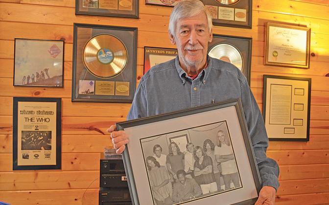 Gary Donehoo holds a photo of him, Alan Walden and Eddie Floyd with Lynyrd Skynyrd in front of his wall of memorabilia of the band. “They were all good guys,” Donehoo said. “The original band, they were hungry, they all came from west Jacksonville… they knew the only way out was education, music or sports.” (Photo/Samantha Sinclair)