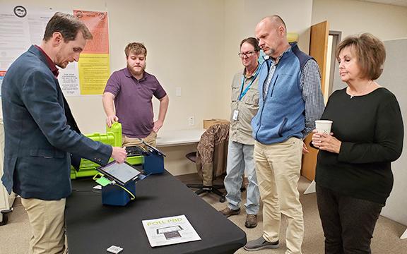 White County Registrar Derek LaPerriere and Habersham Election Technician Izac Martin demonstrate the printers and stands that will help White County speed up the advance voting process to White County Elections and Registration board members Russell Mobley, Todd Marks and Louise Nix. (Photo/Samantha Sinclair)