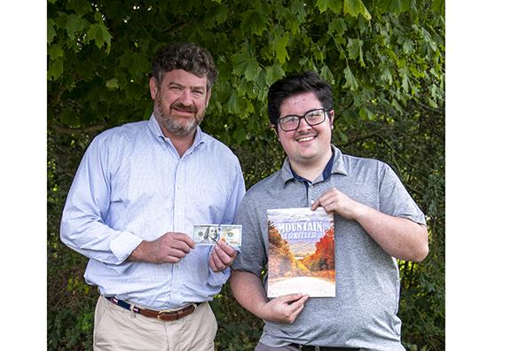 Clarkesville resident Carter Benton receives his $100 prize from Alan NeSmith, Community Newspapers Inc. chairman. Benton’s photo of a street in The Orchard subdivision ablaze with fall colors will grace the cover of the 2023 fall edition of The Mountain Traveler magazine. (Photo/Kimberly Brown)