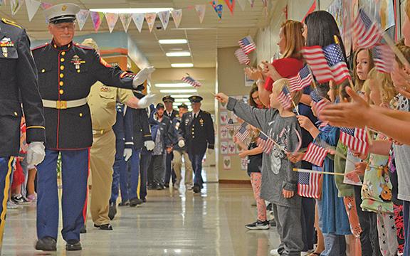 “The photo of the veterans in uniform walking the school halls with students holding flags is so moving, not to mention the depth of the photo ... always a favorite when you feel you are looking into the newspaper, not just a flat image,” judges said of this photo from Veterans Day at Jack P. Nix Elementary School. (Photo/Samantha Sinclair)