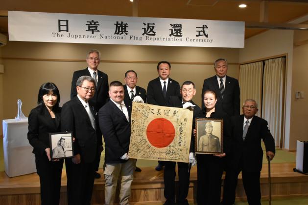 Chris Dorsey, third from left, holds a Yosegaki Hinomaru, a Japanese flag sent to battle with Japanese soldiers during WWII. He’s accompanied by family members of the soldier, Fumio Kudo, and other supporters of the project that returns items to families of soldiers. An unidentified woman holds a picture of Col. Thomas Rogers, great-grandfather of Dorsey, who had the flag for decades. (Photo/submitted)