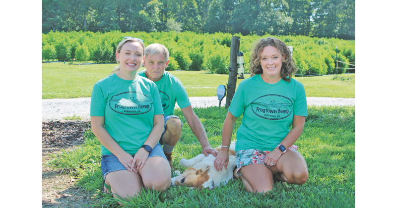 Pictured, from left, Lacey White, Bruce White, Barney the dog and Kelly White enjoy a shady patch of grass on the White Family Barn Farm.