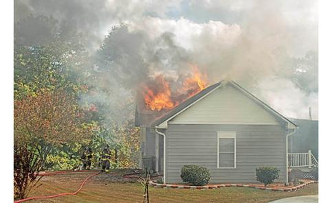 Firefighters work together to contain the fire on Dean Mountain Road as flames burst out of the roof near the garage. (Photo/Noah Johnson)
