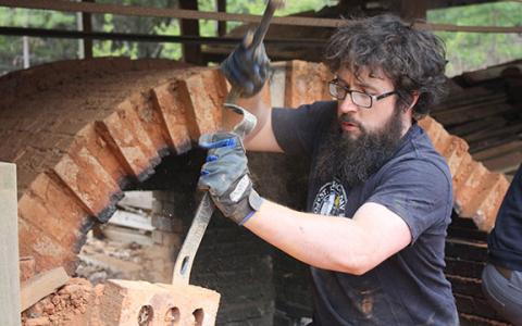 Daniel Bollinger chips away at mortar holding the kiln’s bricks together, digging to pull out any non-eroded bricks he can. (Photo/Eric Tiongson)