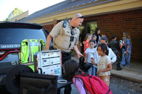 Jack P. Nix Elementary School student Faith Marques examines the equipment on display while School Resource Officer Shawn Blinn offers a vest to student An Duong with Taylen Burnett looking on. PHOTOS BY MAE SULLENS/WCN