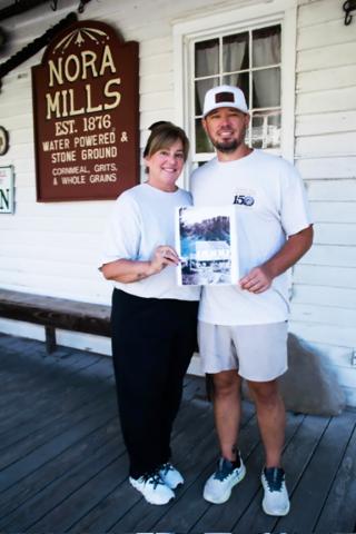 Joann Tarpley, left, and her son Joe Vandergriff, hold an old photo of Nora Mill while standing in front of the grist mill and country store near Helen. SUBMITTED PHOTOS 