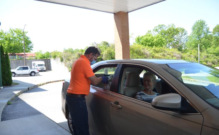 Terry Savoy places a meal in the car of Janelle and James Castleberry as part of the White County Senior Center’s drive-thru pick up service offered during the facility’s closure due to the COVID-19 pandemic. (Photo/Wayne Hardy)