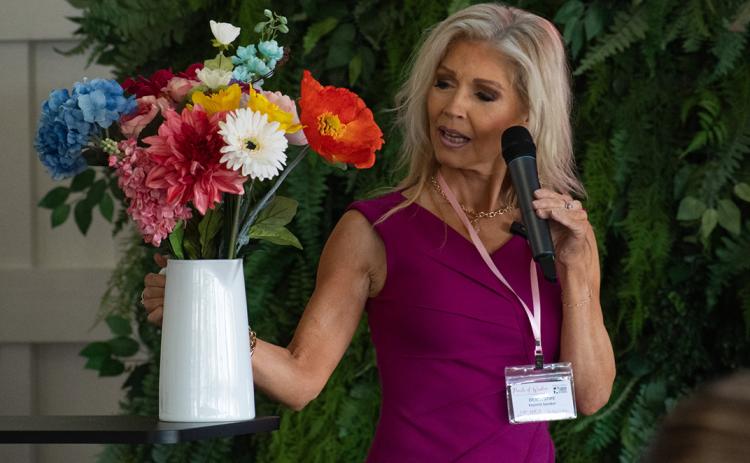 Keynote speaker Debra Stipe holds up a bouquet of different varieties of flowers to illustrate that even though the women in attendance have different talents and career goals, they are brought together as a community to affect the business world with their own brand of innovation and change. Stipe is an entrepreneur, the author of Room to Bloom, and an actress with over 60 professional credits, including her tenure on the popular television series Full House as Cindy. (Photo/Hannah Caudell)