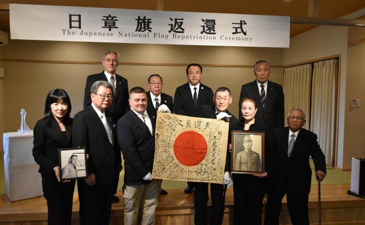 Chris Dorsey, third from left, holds a Yosegaki Hinomaru, a Japanese flag sent to battle with Japanese soldiers during WWII. He’s accompanied by family members of the soldier, Fumio Kudo, and other supporters of the project that returns items to families of soldiers. An unidentified woman holds a picture of Col. Thomas Rogers, great-grandfather of Dorsey, who had the flag for decades. (Photo/submitted)