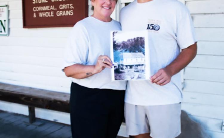 Joann Tarpley, left, and her son Joe Vandergriff, hold an old photo of Nora Mill while standing in front of the grist mill and country store near Helen. SUBMITTED PHOTOS 